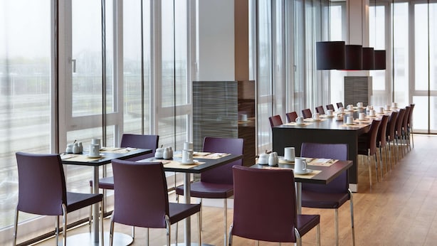 Un comedor moderno con mesas largas y sillas, ventanas amplias y un televisor de pantalla plana.