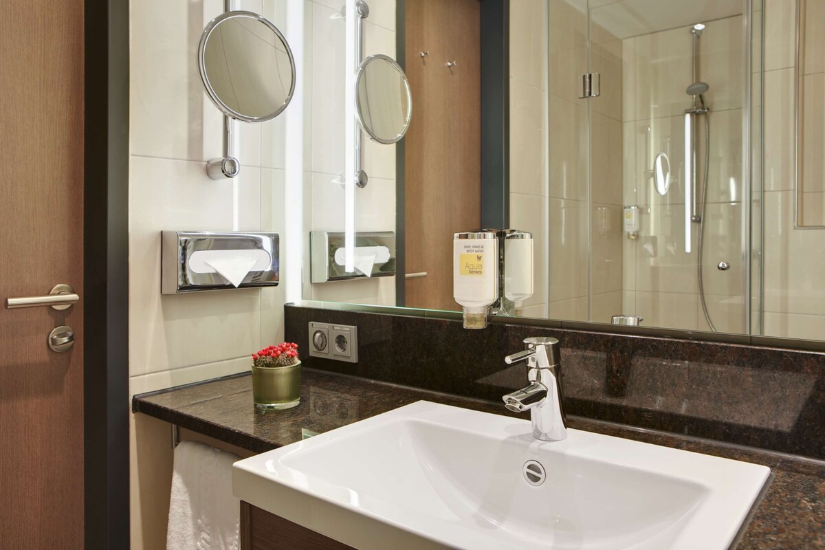 A bathroom with a white sink, two mirrors, a shower, and a towel rack.