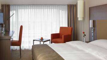 Habitación de hotel con cama, escritorio con silla, una mesita con fruta y una lámpara.