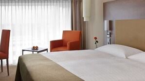 A hotel room with a large bed, a small table with apples, an orange chair, a lamp, and a nightstand with a vase of flowers. - IntercityHotel Darmstadt (Darmstadt)
