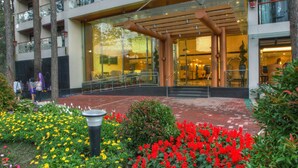 Hotel de diversos pisos amb una entrada central, envoltat d'un jardí amb flors vermelles i grogues.