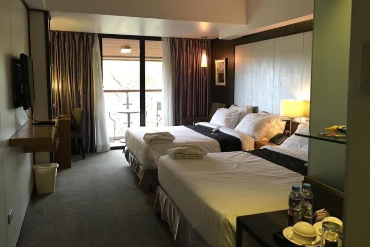 A hotel room with two beds, a desk, a chair, a TV, and a window with curtains.