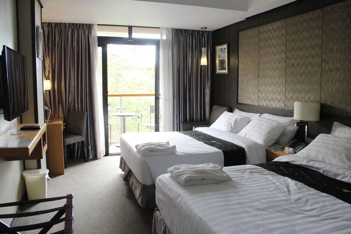 A hotel room with two beds, a desk, a chair, a TV, and a balcony with curtains.