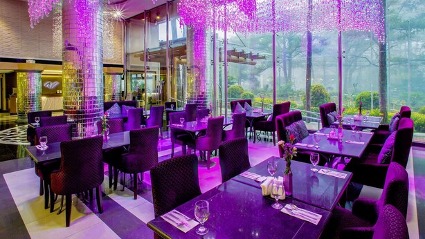 Un restaurant amb il·luminació morada i grans finestres que donen al jardí.