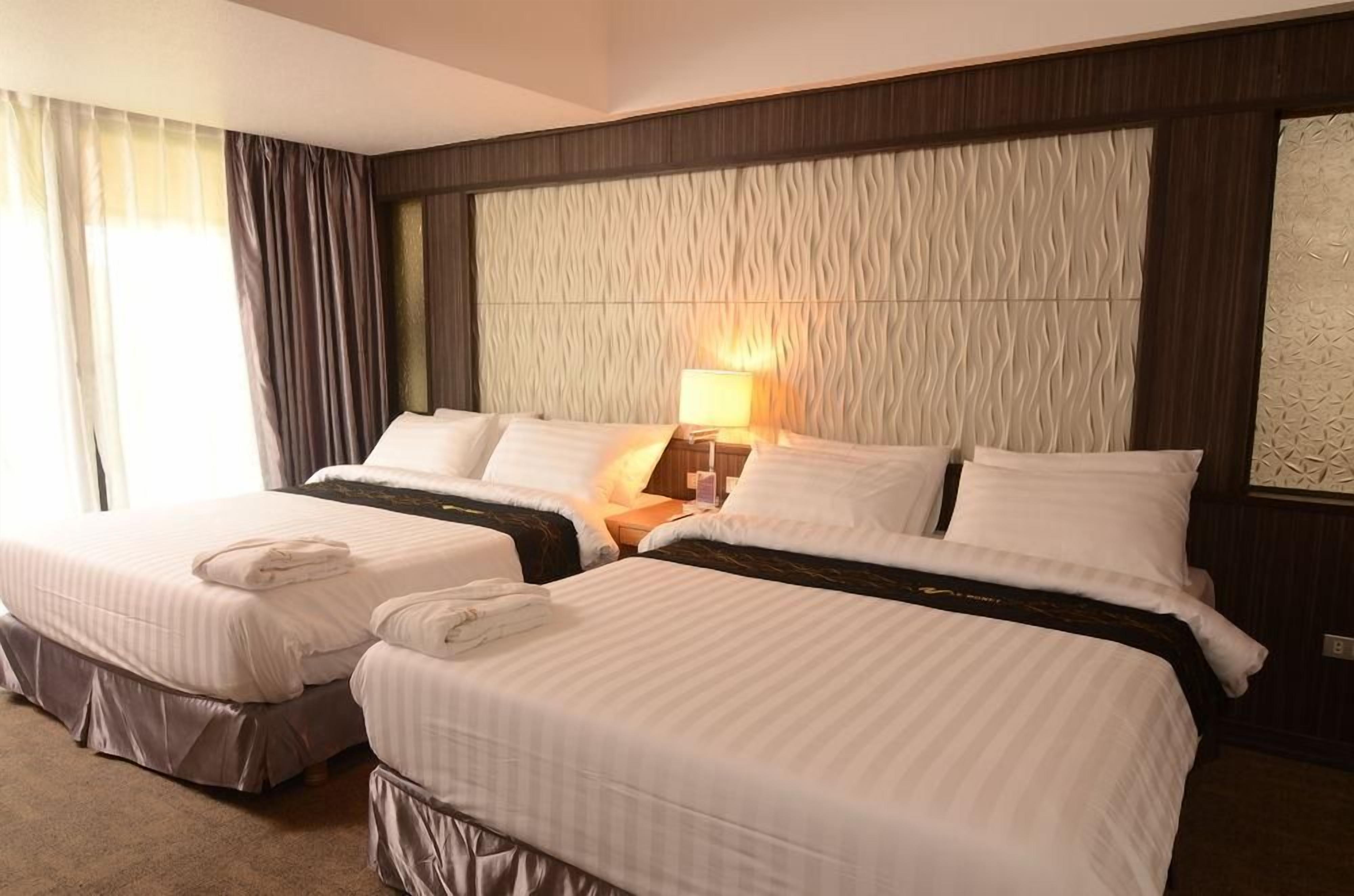 A hotel room with two beds, a nightstand with a lamp, and a large textured wall.