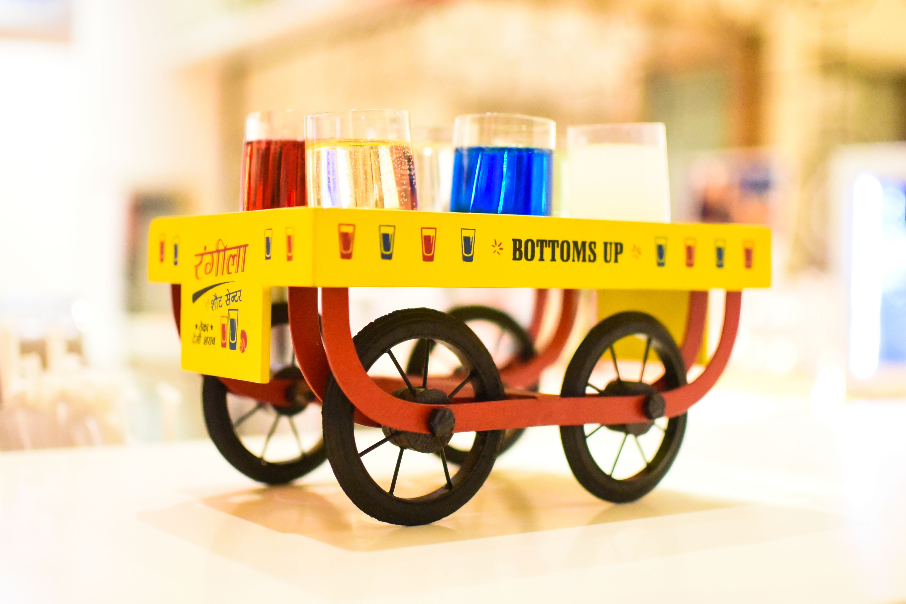 Un carrito con varios vasos de bebidas, con la leyenda 'BOTTOMS UP'.
