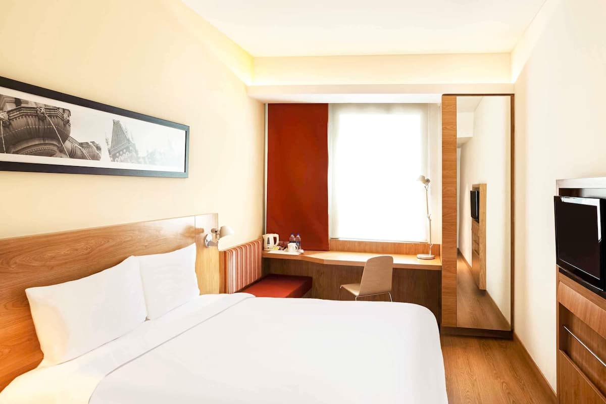 A hotel room with a bed, desk, chair, and a television.