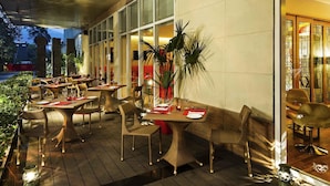 An outdoor dining area with wicker furniture, glass partitions, and potted plants. - ibis Navi Mumbai Hotel (Navi Mumbai)