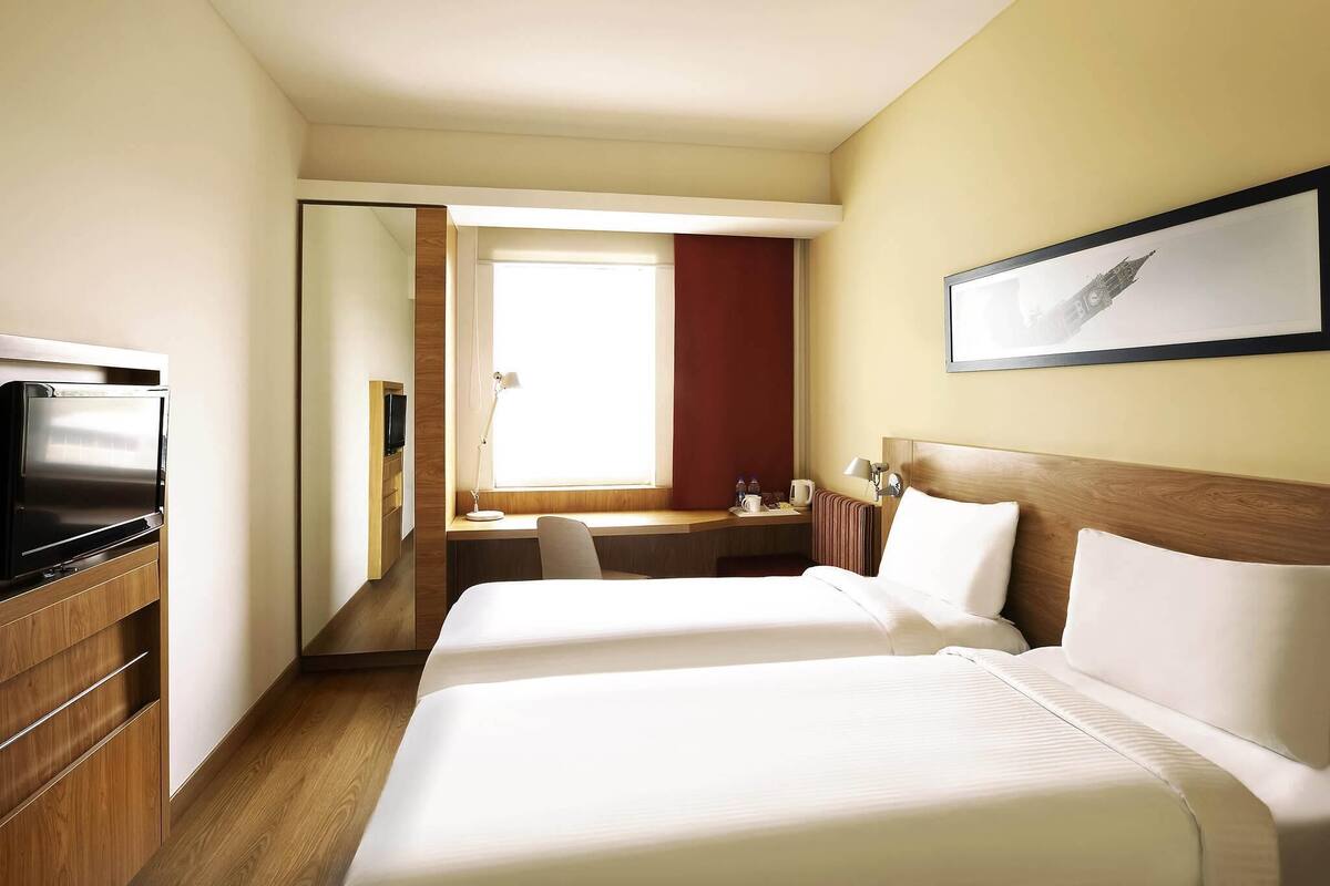 A hotel room with a bed, a desk, a TV, and a window.