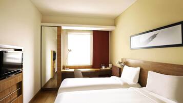 A hotel room with a bed, a desk, a TV, and a window.
