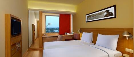 A hotel room with a large bed, a desk, a television, and a window with a view.
