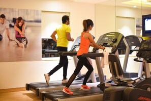Un gimnasio con cintas de correr, un espejo grande y un cartel con gente haciendo ejercicio.