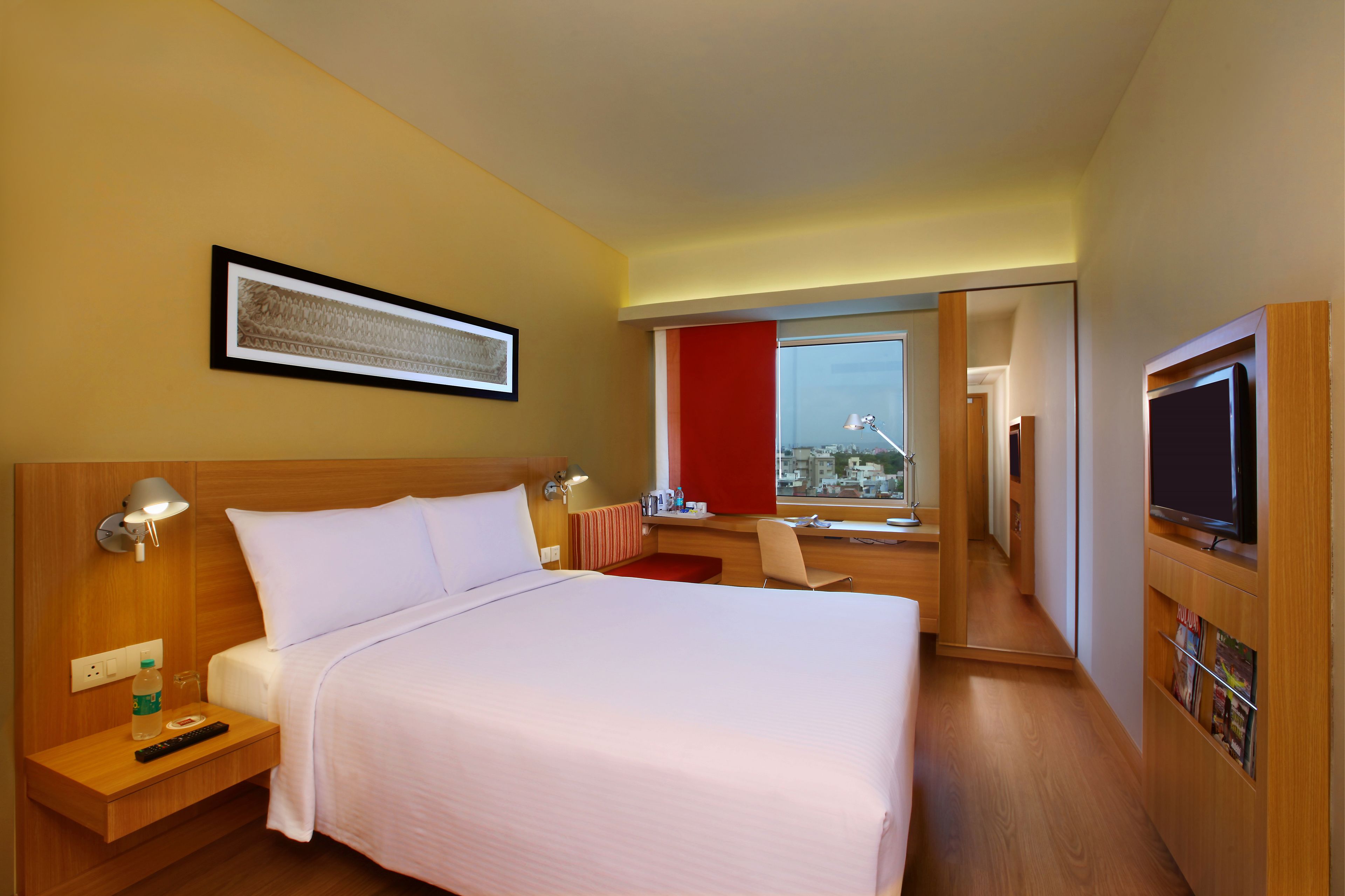 Una habitación de hotel con una cama grande, lámparas de noche, un escritorio con silla, un televisor y una ventana con vista a la ciudad.