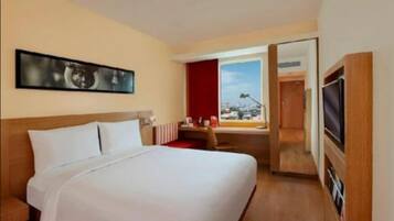 Habitación de hotel con una cama grande, un escritorio, una silla, un televisor y ventana con vista a la ciudad.