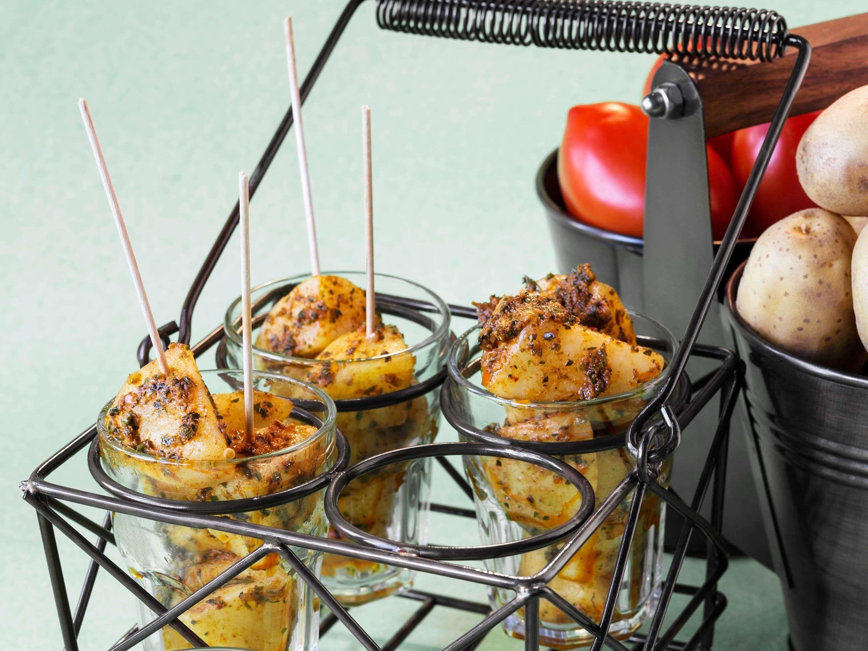 A food display with skewered items in glass containers, a metal rack, and a bucket with potatoes.