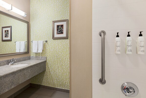 Un baño con lavamanos de encimera de granito, dos cuadros en la pared y tres botellas de productos Alice+O sobre una pared blanca.