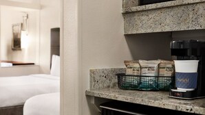 A hotel room with a kitchenette area featuring a coffee maker, a coffee cup, and bags of Rainforest Blend coffee.