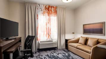 Habitación de hotel con televisión de pantalla plana, sofá de cuero, escritorio con silla, ventana grande con cortinas y un cuadro en la pared.