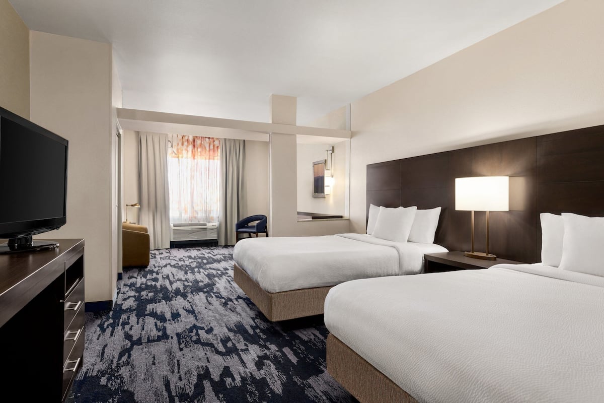 A hotel room with two beds, a TV, a desk, and a window with curtains.