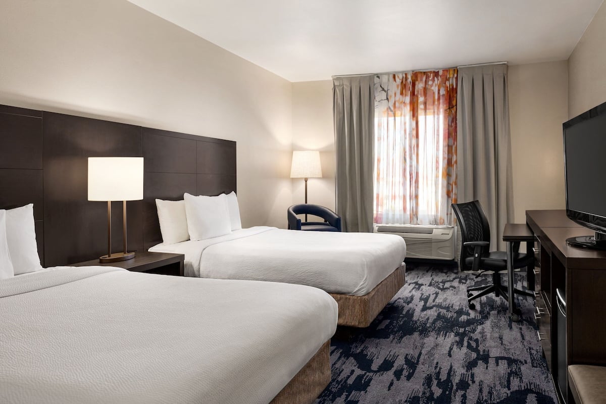 A hotel room with two beds, a desk, a chair, a TV, and a window with curtains.