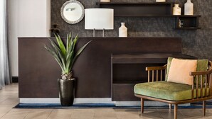 A reception area with a dark wooden reception desk, a green cushioned chair, a potted plant, and a wall-mounted mirror.