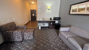 A hotel room with a patterned carpet, a sofa, a small table, a microwave, and a sink. - Comfort Inn & Suites (Fort Saskatchewan)