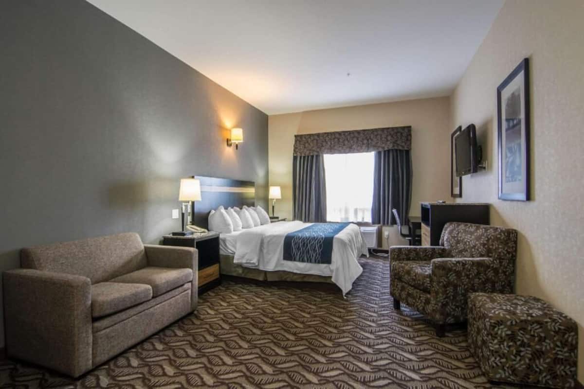 A hotel room with a bed, two armchairs, a sofa, a desk, a lamp, a TV, and a window with curtains.