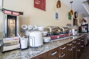 A breakfast buffet setup with multi-grain and original options, a coffee machine, and a clock on the wall.