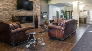 A lobby with leather sofas, a flat-screen TV, a fireplace, and a stone wall. - Comfort Inn & Suites (Fort Saskatchewan)