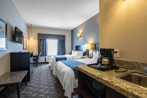 Habitación de hotel con dos camas, un escritorio, una silla, una cafetera y un lavamanos.
