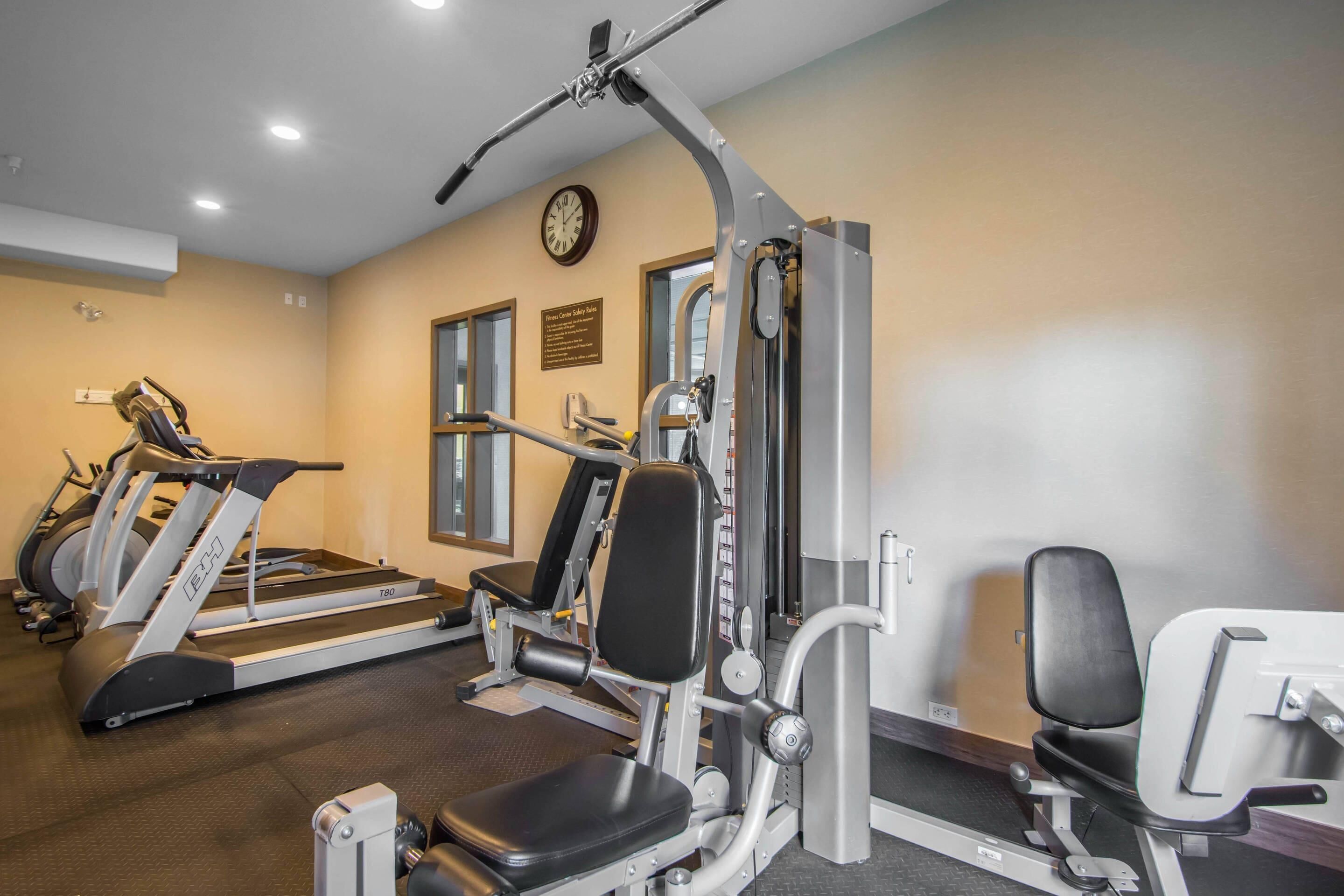 Un gimnasio con cintas de correr, máquinas de pesas y un reloj de pared.