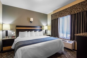 Habitación de hotel con una cama grande, dos mesitas de noche con lámparas, un calentador en la pared y una ventana con cortinas.