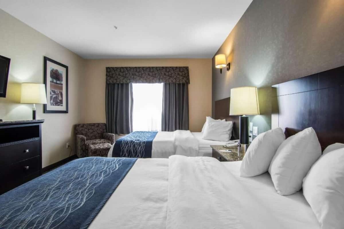 A hotel room with two beds, a desk, a chair, a TV, and a window with curtains.