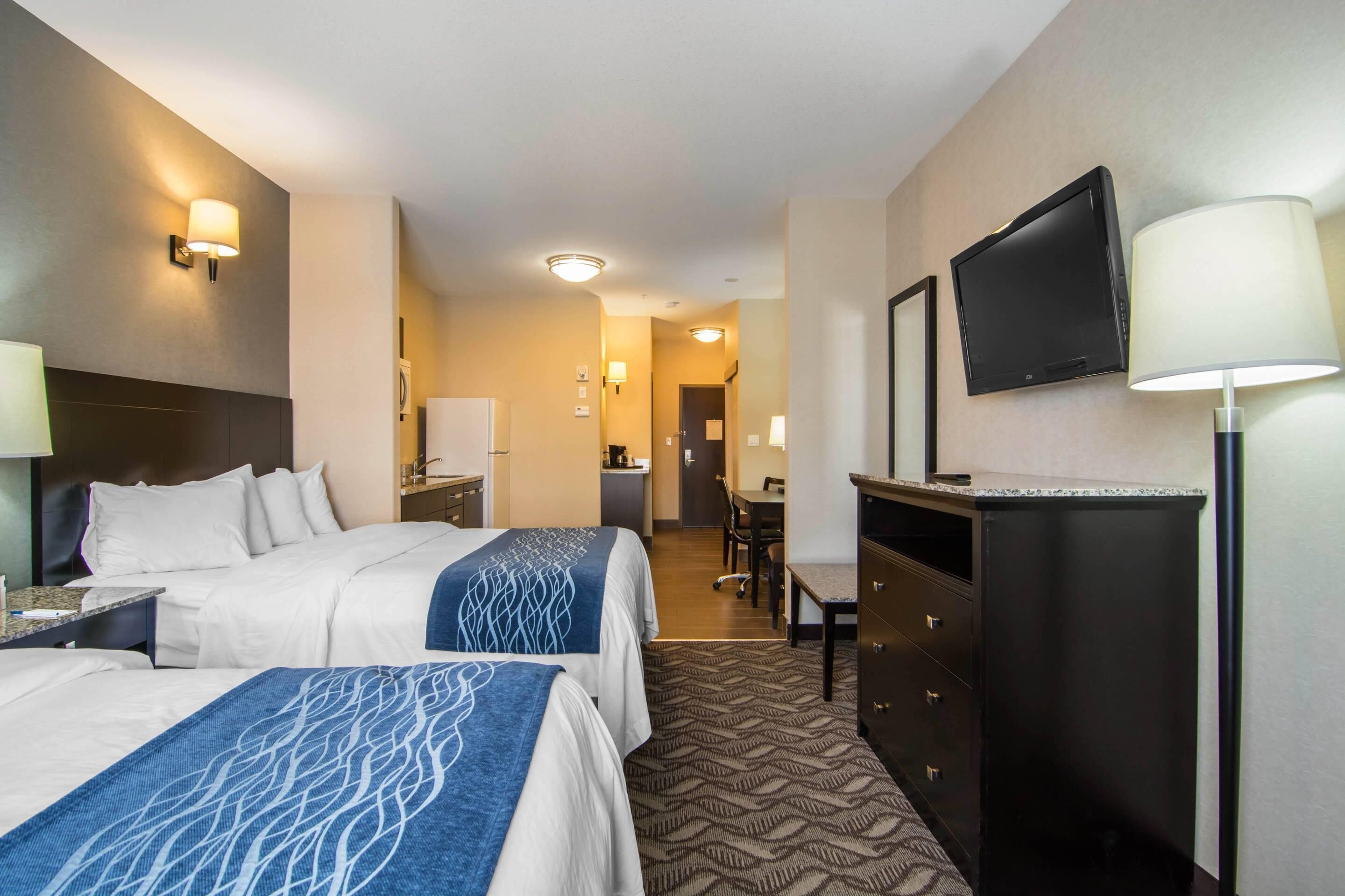 A hotel room with two beds, a desk, a television, and a dresser.