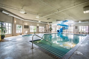 An indoor swimming pool with a blue slide, large windows, and a ceiling with visible ductwork.