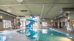 An indoor swimming pool with a blue slide, lounge chairs, and a view of the outdoors. - Comfort Inn & Suites (Fort Saskatchewan)