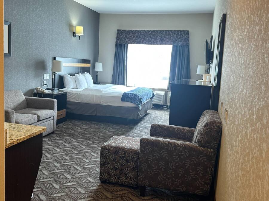 Habitación de hotel con una cama, dos sillones, un escritorio, un televisor y un ventanal con cortinas.