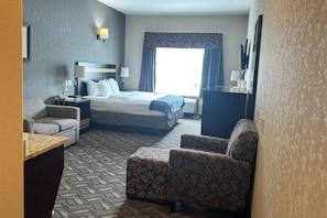 Habitación de hotel con una cama, dos sillones, un escritorio, un televisor y un ventanal con cortinas.