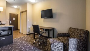 A hotel room with a kitchenette, a flat-screen TV mounted on the wall, a desk, and two patterned armchairs. - Comfort Inn & Suites (Fort Saskatchewan)