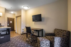 A hotel room with a kitchenette, a flat-screen TV mounted on the wall, a desk, and two patterned armchairs. - Comfort Inn & Suites (Fort Saskatchewan)