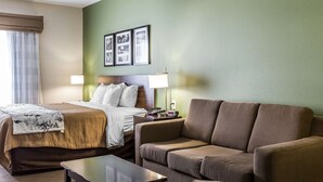 A hotel room with a bed, a sofa, a nightstand, a lamp, and framed pictures on the wall. - Sleep Inn & Suites Mount Olive North (Mount Olive)