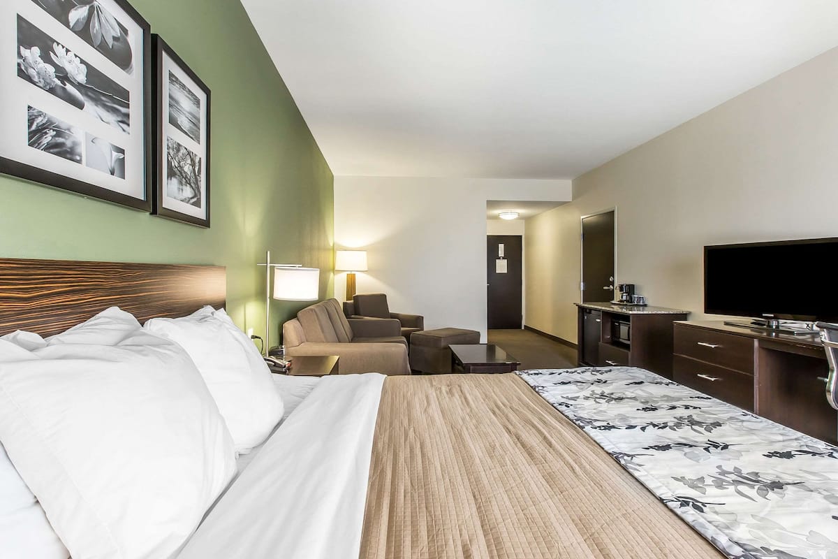 Ein Hotelzimmer mit Bett, Sofa, Fernseher, Schreibtisch und Kaffeemaschine.