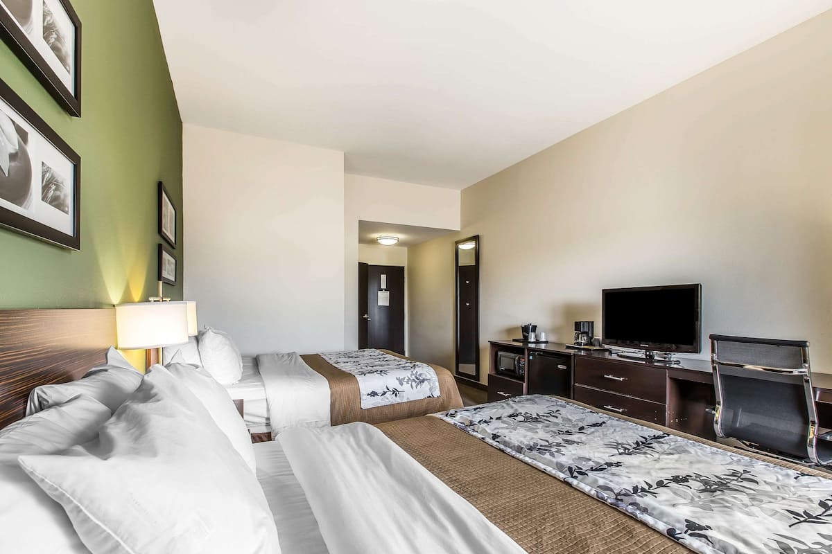 Ein Hotelzimmer mit zwei Betten, einem Fernseher, einem Schreibtisch und einem Spiegel.