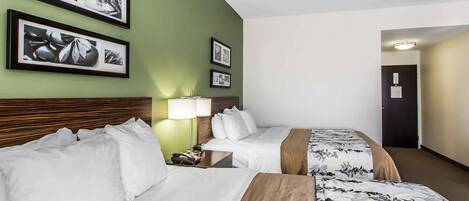 Habitación de hotel con dos camas, un cabecero de madera, una mesita de noche con lámpara y cuadros enmarcados en la pared.
