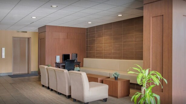 A modern lobby with a sofa, chairs, a small table, and a potted plant. - New Lodge (Winnipeg)