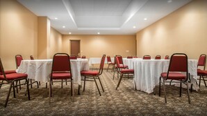 A conference room with multiple tables and red chairs, carpeted floor, and beige walls. - New Lodge (Winnipeg)