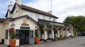 Un edificio con un letrero que dice 'The Highwayman' y 'Hungry Horse' a la izquierda. Hay macetas grandes y cestas colgantes de flores en la fachada.