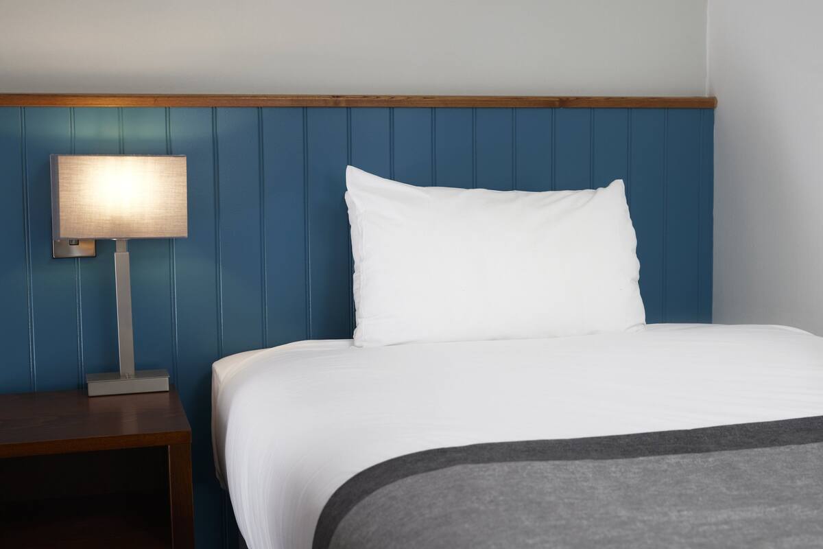 A neatly made bed with white bedding, a wooden headboard, and a bedside table with a lamp.