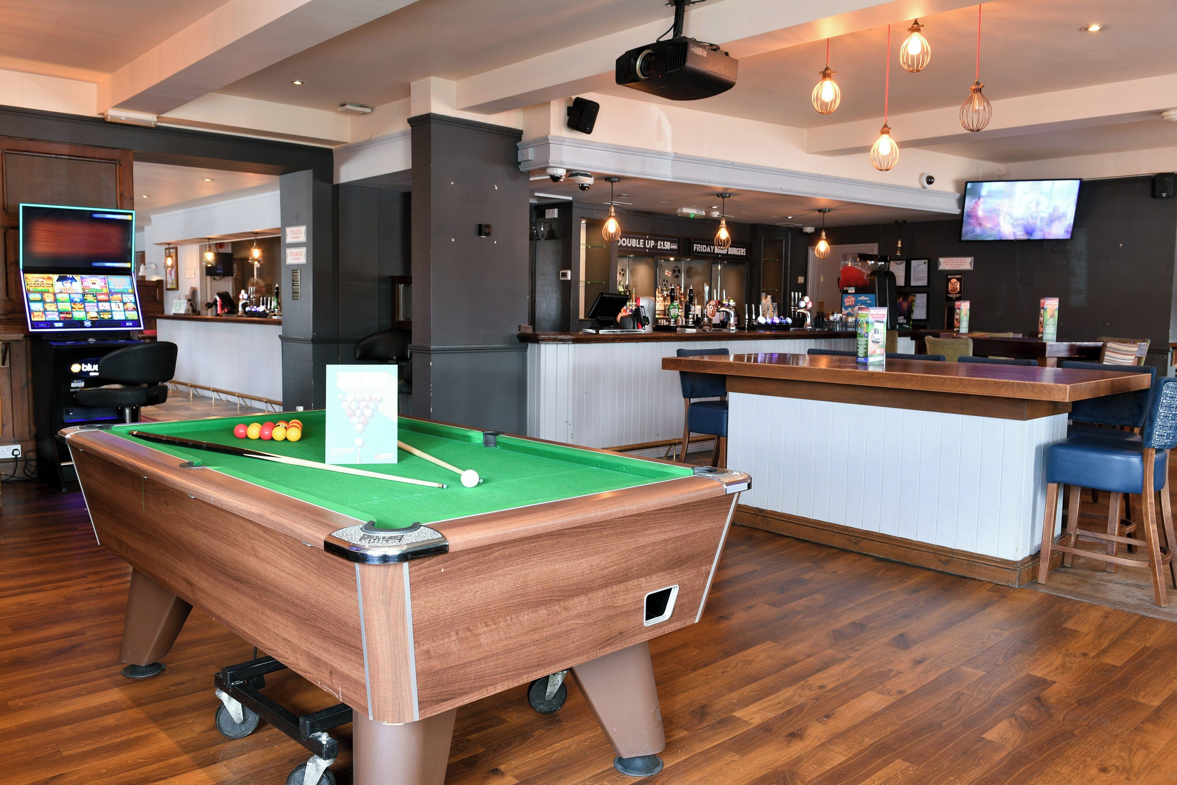 A pool table with balls, a bar area with a TV, and a billiard cue rack.