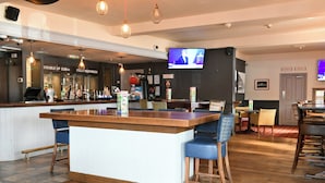Una zona de bar con mostrador de madera, taburetes, una pantalla de televisión y un cartel que dice 'DOUBLE UP - £15'.
